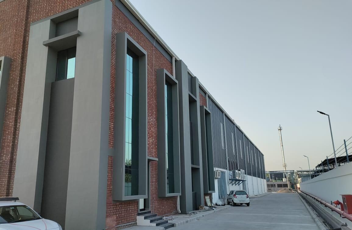 “Contemporary factory construction with exposed brick and glass facade by Arpit Constructions”